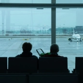 Dos personas esperan sentadas frente a un avión aparcado en la pista del aeropuerto. David Zorrakino / Europa Press