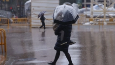 Personas caminan ante ninots tapados con plásticos por la lluvia durante el montaje de las Fallas 2026, en la plaza del Ayuntamiento, a 5 de marzo de 2026, en Valencia, Comunidad Valenciana (España). Rober Solsona / Europa Press.