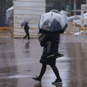 Personas caminan ante ninots tapados con plásticos por la lluvia durante el montaje de las Fallas 2026, en la plaza del Ayuntamiento, a 5 de marzo de 2026, en Valencia, Comunidad Valenciana (España). Rober Solsona / Europa Press.
